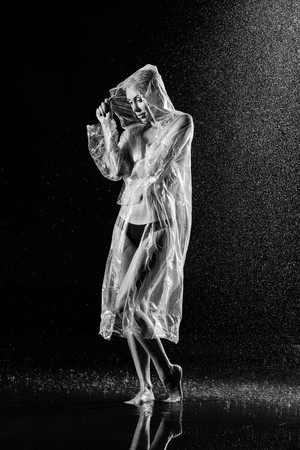 Nuded girl in raincoat standing in the rain. Black and white. Photographie retoucheeの写真素材