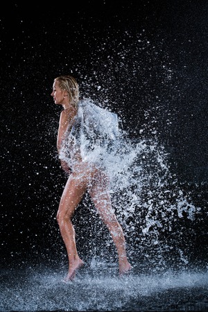 Nuded girl pulling pocket in water splashes. Black background. Photographie retoucheeの写真素材