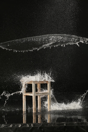 Vintage wooden stool and splashes of water. Black backgroundの写真素材