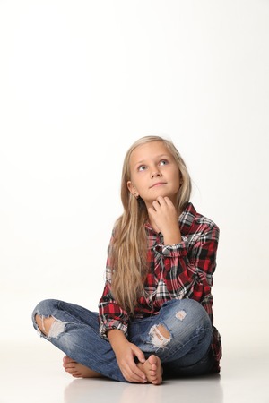 Girl with long blond hair sits thoughtfully on the floor. White backgroundの写真素材