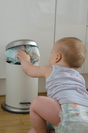baby touching the garbage can full of  used dirty diapers.  view from back. selective focus   .の写真素材