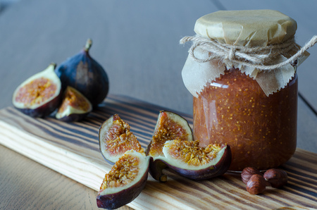 Closed glass jar of Fig jam, nuts and sliced figs on a wooden table backgroundの写真素材