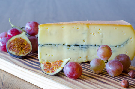 A big piece of cheese, grapes, nuts, sliced figs on wooden table background. close up.の写真素材