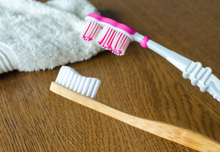 Bamboo toothbrush vs plastic toothbrush with towel on the wooden backgroundの写真素材