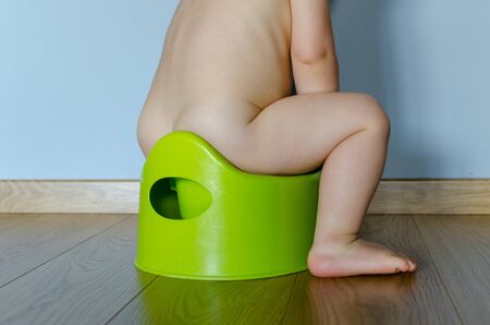 Funny baby boy sitting on chamberpot. Children's legs hanging down from a chamber-pot. Side viewの写真素材