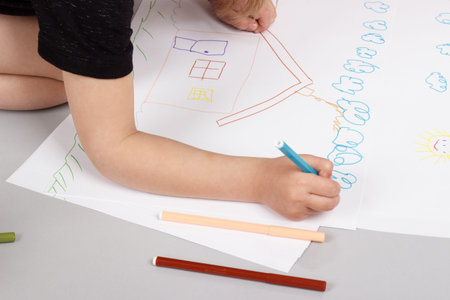 The little girl draws felt-tip pens house on a gray background