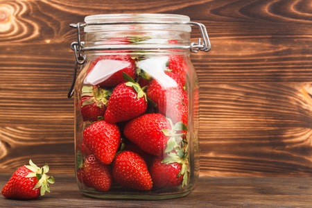 Red strawberries inside the glass jar on the wooden backgroundの写真素材