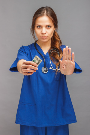 Woman doctor in the blue medical uniform and with money in the hand, gray backgroundの写真素材