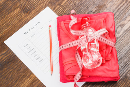 Sports items: Sports clothing, tape measuring and list of diet plan on the wooden background
