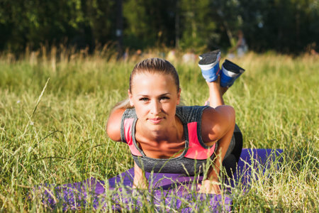 Young attractive woman makes sport exercise outdoors, soft focus background