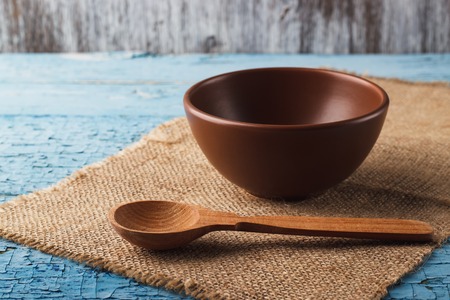 Clay brown dish for food with a wooden spoon on old wooden tableの写真素材