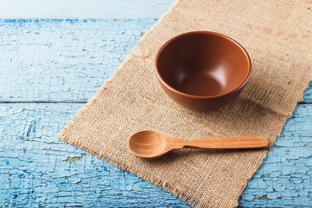 Brown ceramic bowl and wooden spoon on the napkin from burlap, wooden tableの写真素材