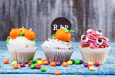 Halloween cupcakes with decorations: tombstone, eyes and pumpkins made from confectionery mastic, soft focus backgroundの写真素材