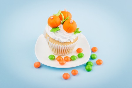 Halloween cupcake with decorations: orange pumpkins made from confectionery mastic on the plate, light blue backgroundの写真素材