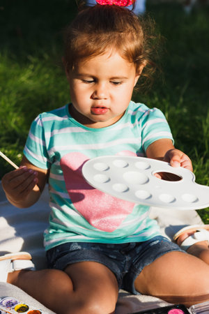Small girl holds a palette of watercolor and paintbrush, soft focus backgroundの写真素材