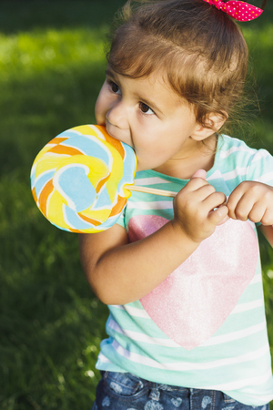 Small cheerful girl with colored candy outdoors, soft focus backgroundの写真素材