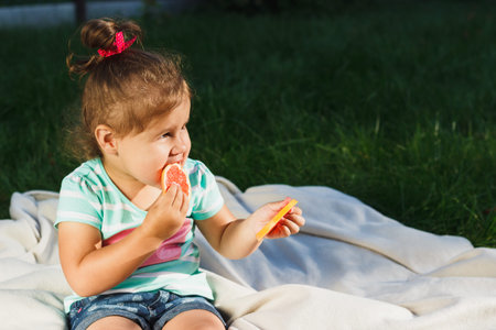 Small girl sitting and holds a slice of fresh grapefruit, soft focus backgroundの写真素材