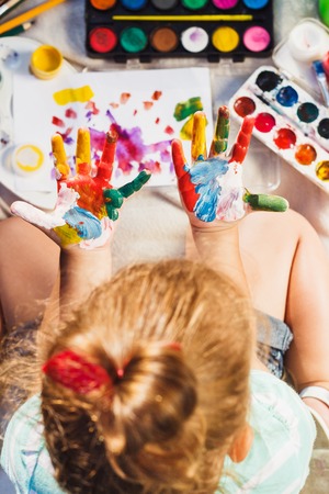 Small girl shows painted colorful hands, soft focus backgroundの写真素材