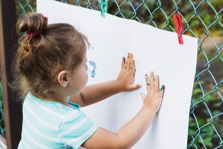 Small girl draws by her painted colored hands, soft focus backgroundの写真素材