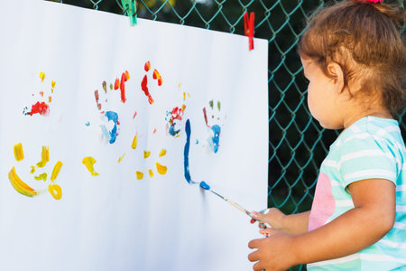 Small girl holds paintbrush and draws by watercolors, soft focus backgroundの写真素材