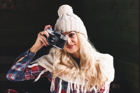Woman blonde in the knitted hat takes a picture on the old camera, soft focus backgroundの写真素材