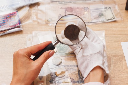Woman looking at the old coin through a magnifying glass, soft focus backgroundの写真素材