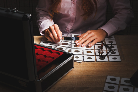 Woman looking at the coins through a magnifying glass, soft focus backgroundの写真素材