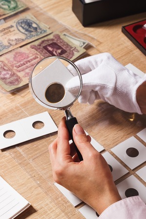 Woman looks at the coin through a magnifying glass, soft focus backgroundの写真素材