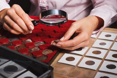Woman looks at the coin through a magnifying glass, soft focus backgroundの写真素材