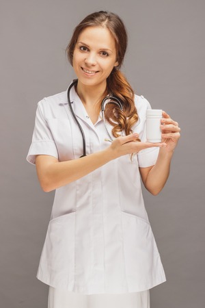 Woman doctor in the white medical uniform with a jar of pills in the hands, gray backgroundの写真素材