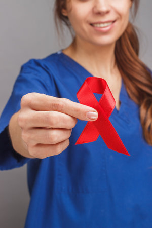Woman doctor in the blue medical uniform with a red ribbon in the hand, gray background