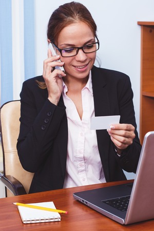 Business concept: woman talking by the phone in the office and holds a card in the hand, soft focus backgroundの写真素材