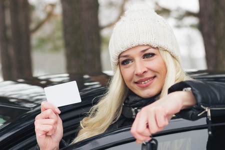 Concepts of buying or rental car: woman with car keys and card in the hands standing near the black car, winter forest, soft focus backgroundの写真素材