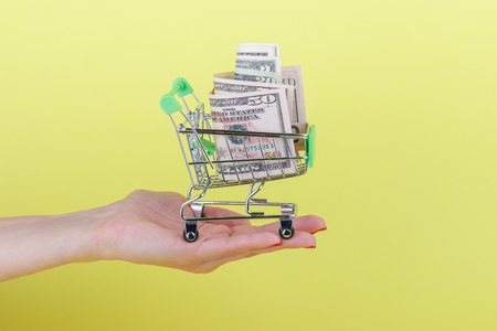 American dollars in the shopping pushcart, on the yellow backgroundの写真素材