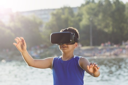 The boy plays game with virtual reality glasses outdoors. Digital vr deviceの写真素材