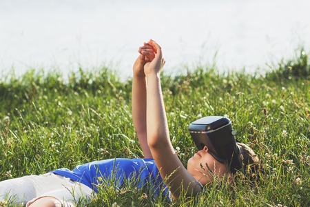 The boy plays game with virtual reality glasses outdoors. Digital vr deviceの写真素材
