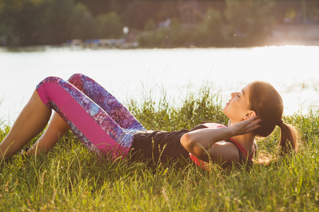 Sporty attractive woman on the lakes coast makes sport exercises on the sunset, soft focus backgroundの写真素材