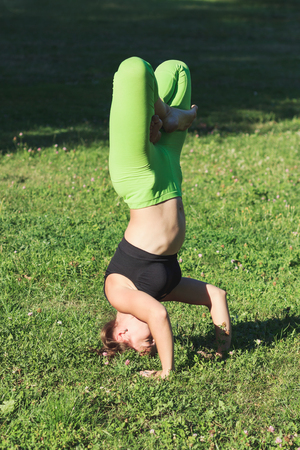 Woman makes yoga exercises on the green grass in the park, soft focus backgroundの写真素材