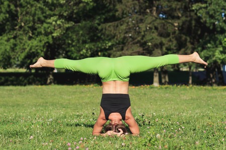 Woman makes yoga exercises on the green grass in the park, soft focus backgroundの写真素材