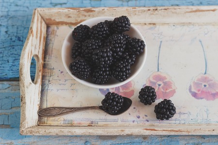 Blackberry in the white bowl with a spoon on the wooden tray, soft focus backgroundの写真素材