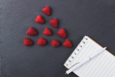 Red raspberries, notebook and a pen on the black slate stone background, top viewの写真素材