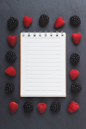 Red raspberries, tape measure, notebook and a pen on the black slate stone background, top viewの写真素材