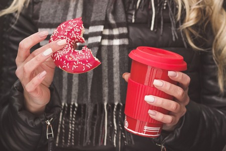 Cup of hot drink and red donut in the woman's hands, soft focus backgroundの写真素材