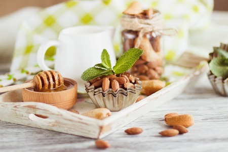 Honey in the wooden bowl, mint leaves, almonds and jar with milk on the wooden tray, soft focus backgroundの写真素材