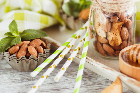 Honey in the wooden bowl, mint leaves, almonds and jar with milk on the wooden tray, soft focus backgroundの写真素材