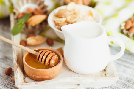 Honey in the bowl, muesli, mint leaves, almonds and jar with milk on the wooden tray, soft focus backgroundの写真素材