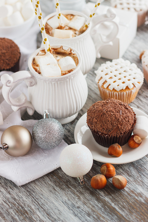 Cups with cacao and marshmallow, cupcakes and different Christmas decorations, soft focus backgroundの写真素材