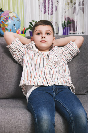 Smiling boy with a phone sits on the sofa, indoors, soft focus background