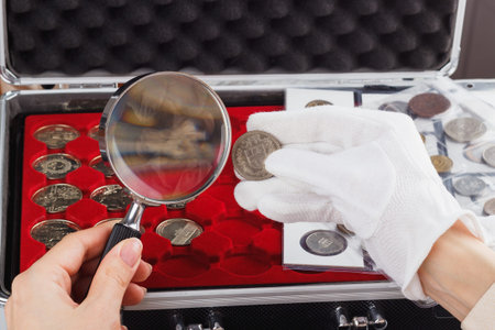 Woman with a magnifying glass and gold coin in the hand, soft focus backgroundの写真素材