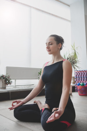 Beautiful woman makes the yoga exercise on the mat, indoors, soft focus background